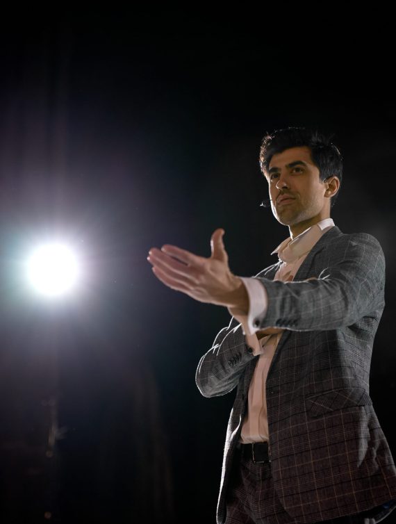 Successful Motivational Speaker In Suit Talking about Happiness, Self, Success, Improvement, Efficiency, Health, and How to Be More Productive. Male Gesturing. Large Conference Hall Stage